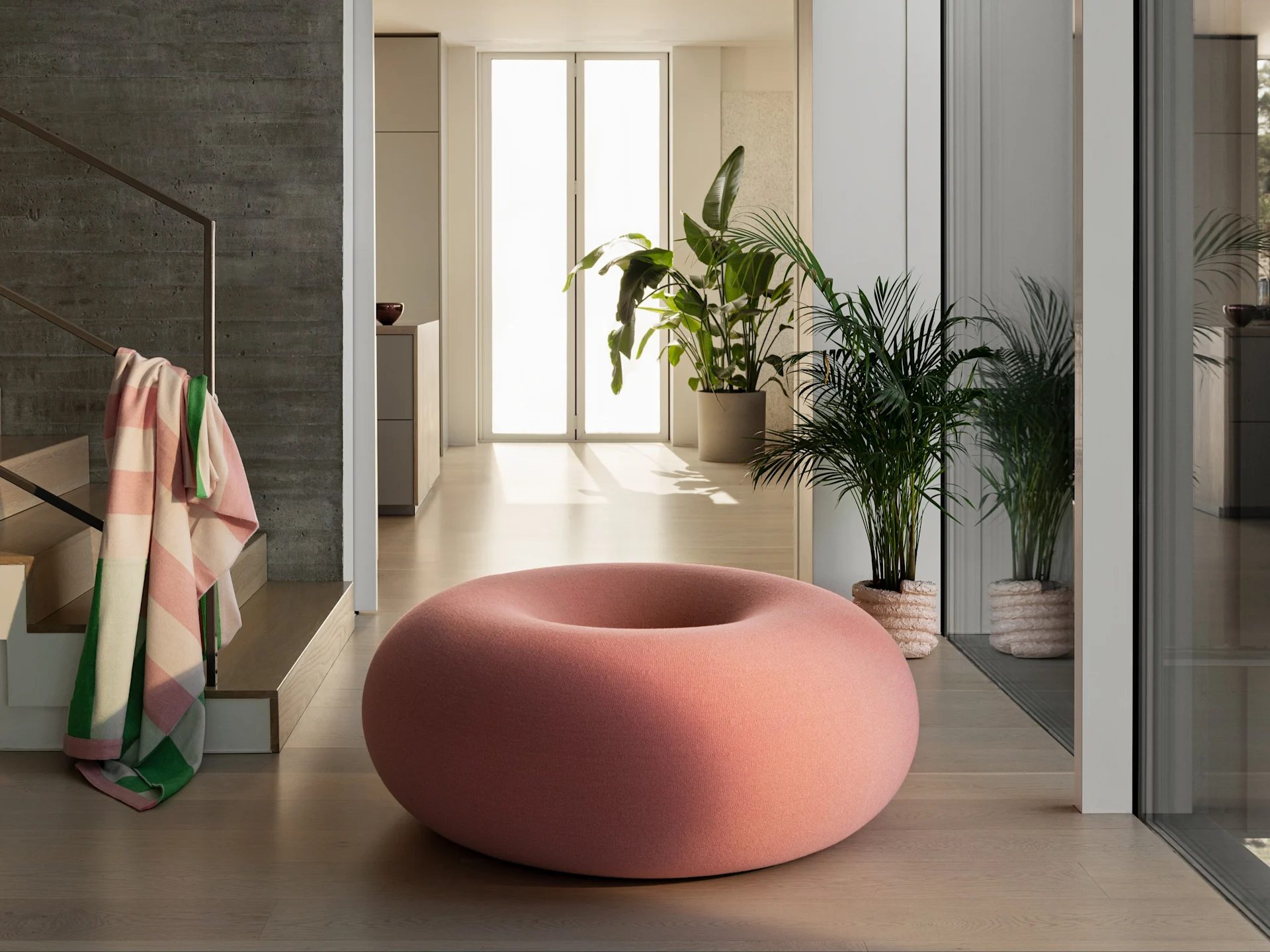 En stor, smultringformet rosa puff på et lyst tregulv i et moderne rom med grønne planter og en betongvegg.