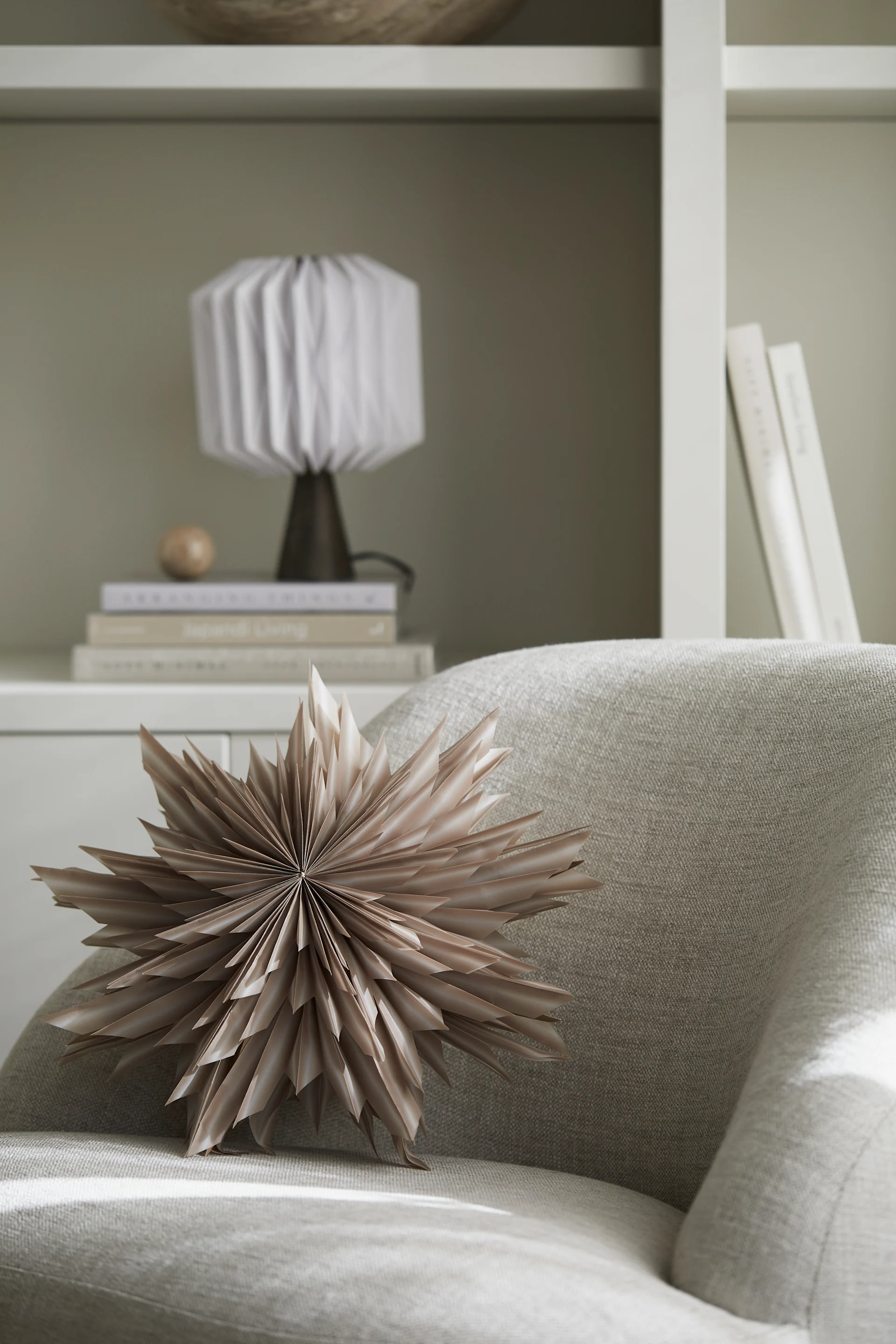 En Helena adventsstjerne i papir fra Watt & Veke ligger på en lenestol, klar til å henges opp.
