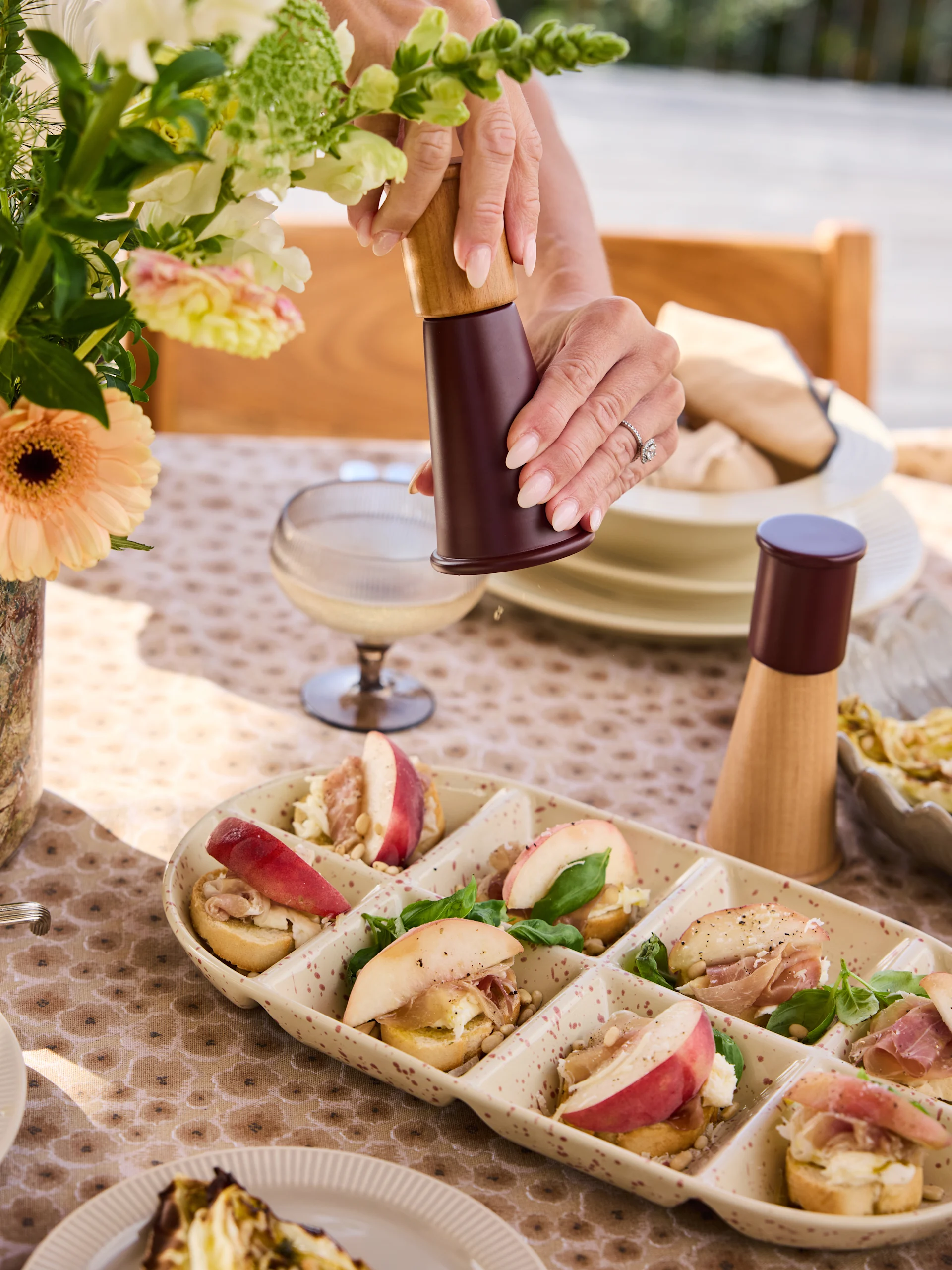 Hender kverner pepper på crostini-fat med fersken, prosciutto, ost, pinjekjerner, basilikum.