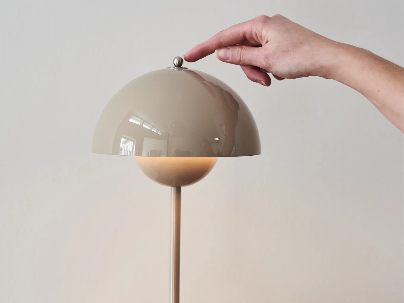 Hånd trykker på en metallisk knapp på en beige kuppelformet lampe, som avgir et varmt lys.