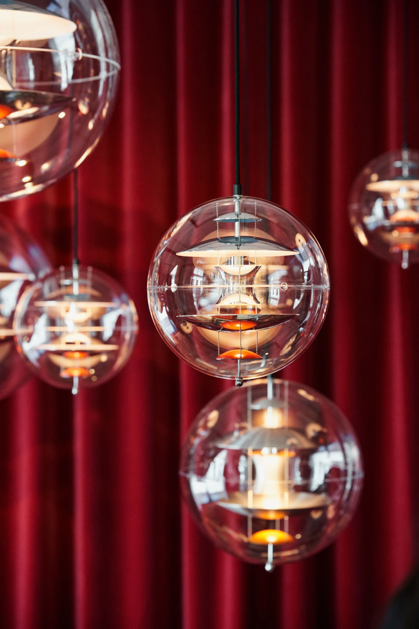 Flere Globe Glass-pendellamper fra Verpan henger fra taket foran et rødt gardin.
