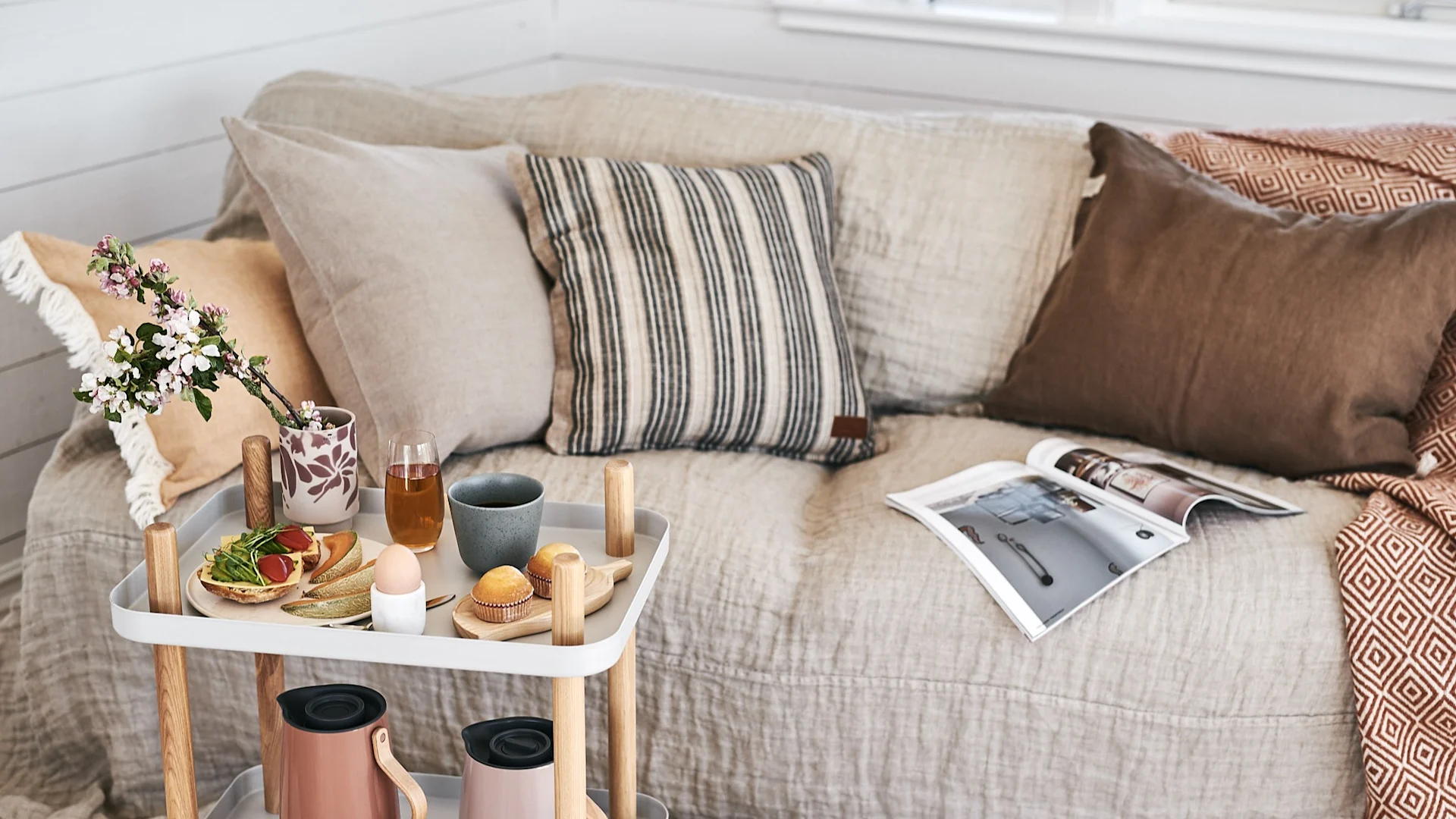 En luksusfrokost serveres på sidebord fra Normann Copenhagen og sofaen inviterer til avslapning med myke puter fra ERNST og et varmt terrakottapledd.