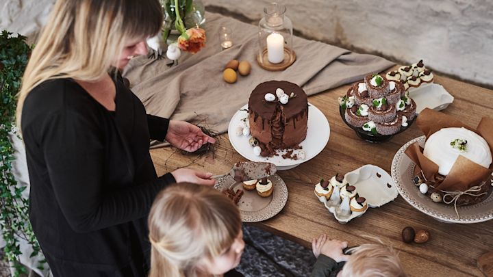 Et rustikk påskebord med flere forskjellige påskedesserter, som sjokoladekake som gjestene skjærer et stykke av.