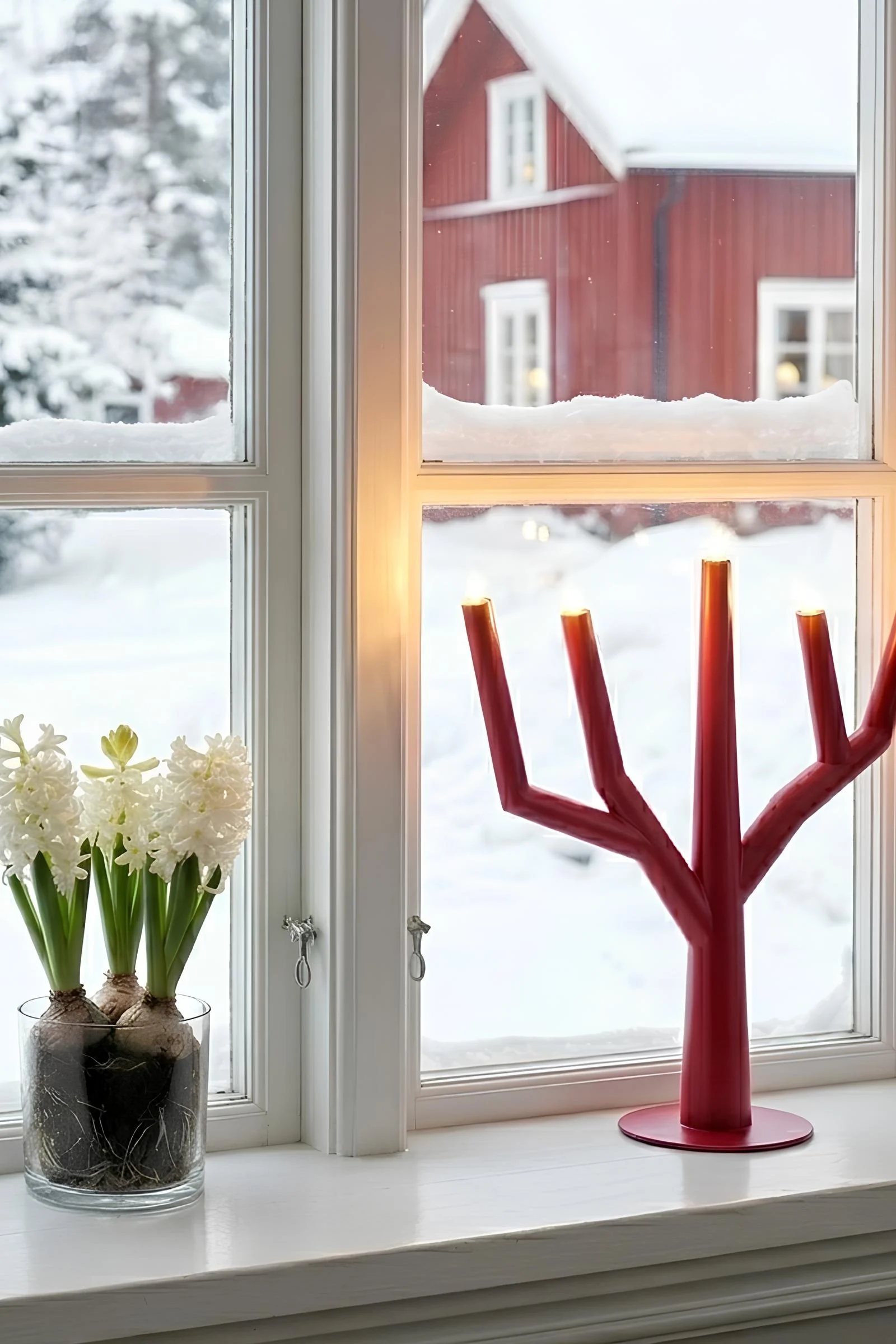 To A-formede lysestaker, en svart, en hvit, med tente elektriske lys på et trebord ved siden av en vase med en furugren.