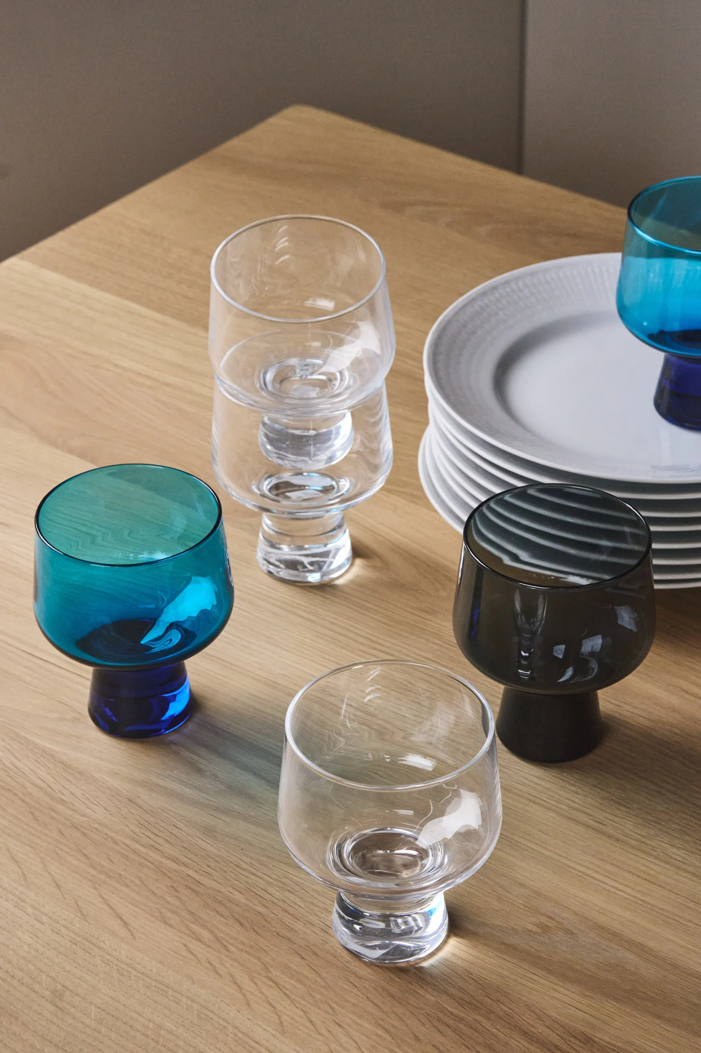Her ser du en samling glass fra Solare-kolleksjonen til Iittala, sammen med en stabel hvite tallerkener.