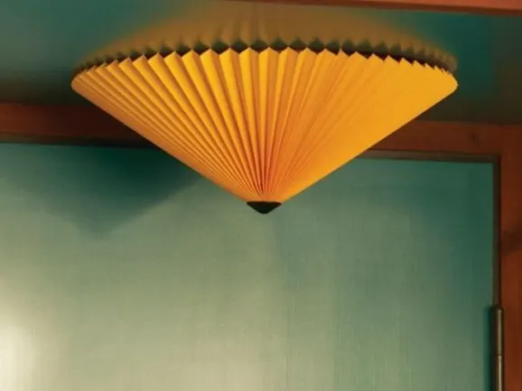 Gul plissert konisk taklampe mot en turkis vegg.