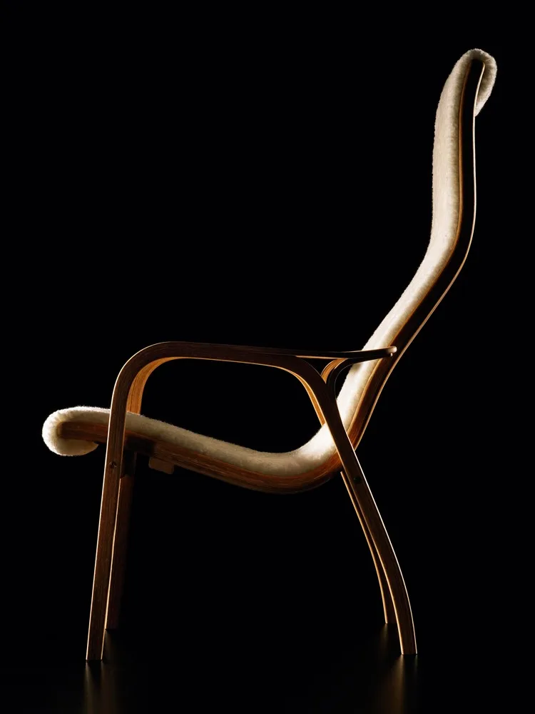 En elegant loungestol med buet lyst treverk og kremfarget pelsbekledning, mot en svart bakgrunn.