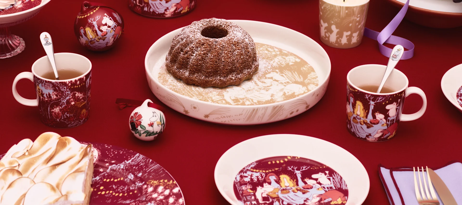 Flere ulike mummikopper fra Moomin Arabia står på et bord ute, ved siden av en presskanne.
