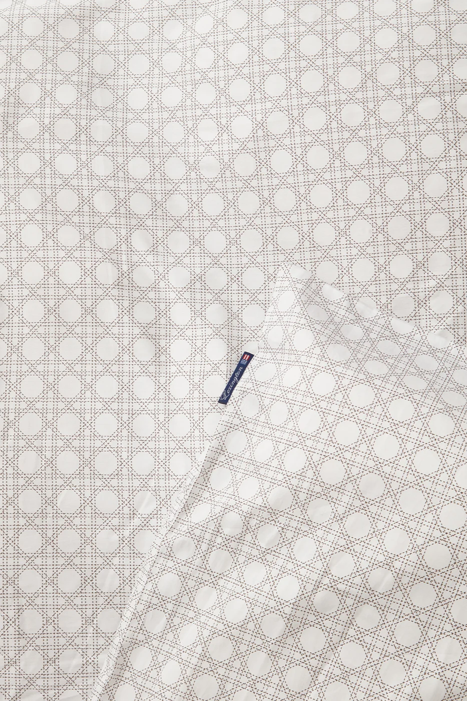 Hvitt stoff med lys brunt flettverksmønster og en blå Lexington-etikett.