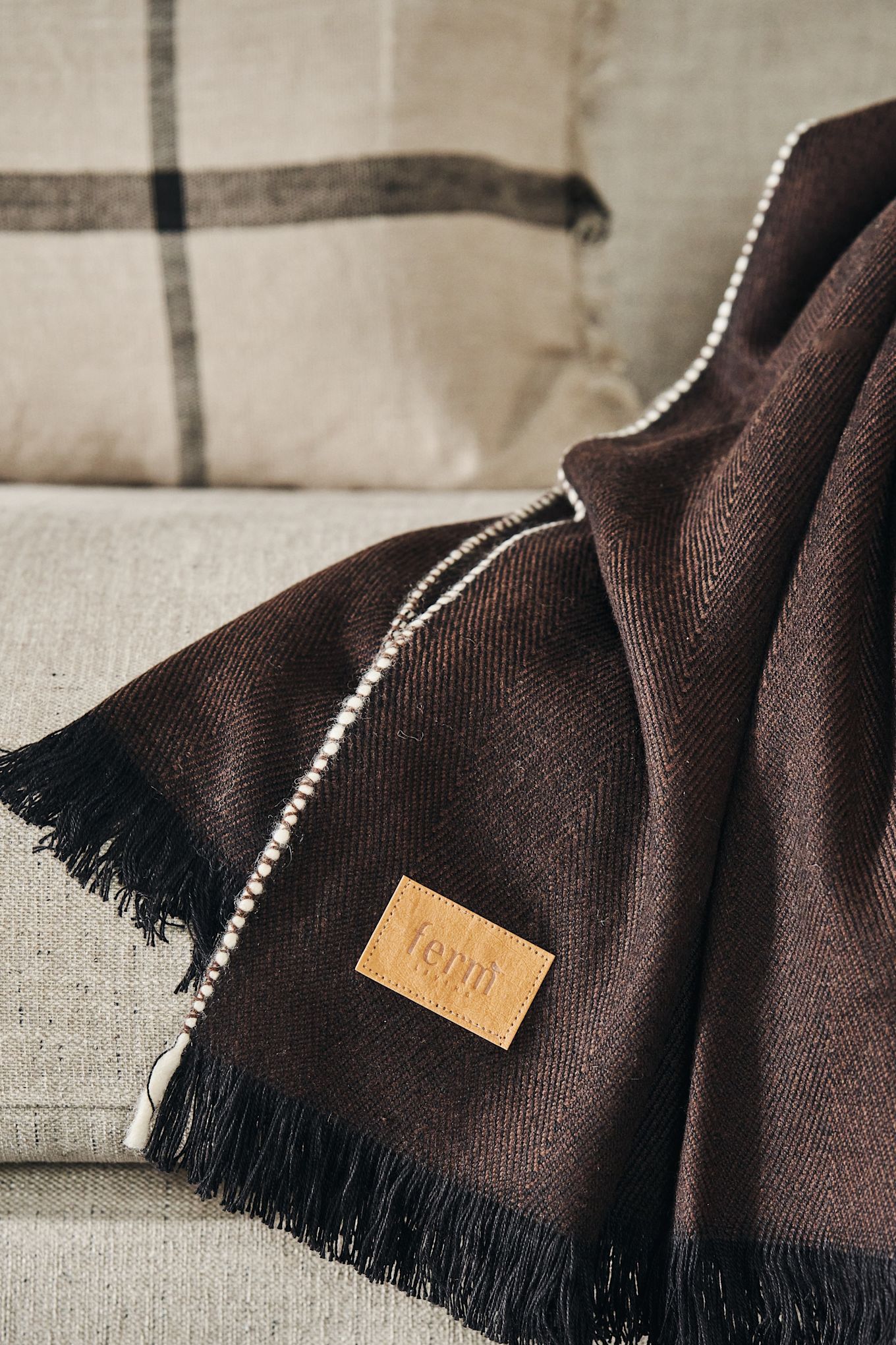 Herringbone pledd i mørkebrunt fra Ferm Living med den vakre etiketten i fokus. 