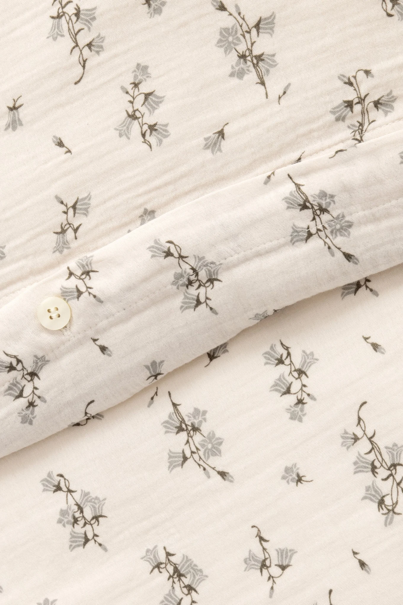 Nærbilde av kremfarget stoff med grått klokkeblomstmønster og en hvit knapp.