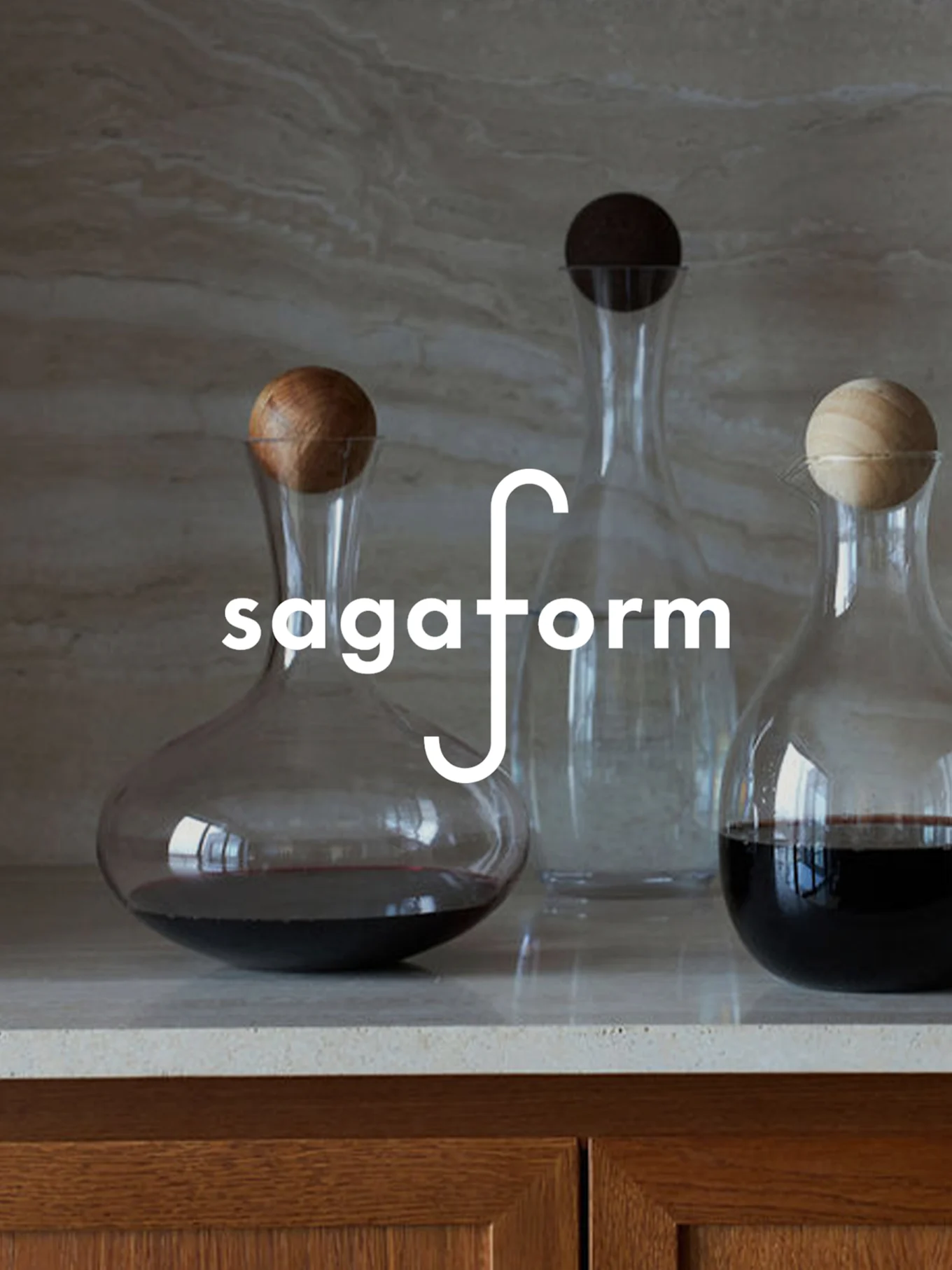 Tre glasskarafler med sfæriske trekorker på en benkeplate, to inneholder rødvin. Logoen "sagaform" er overlagt.