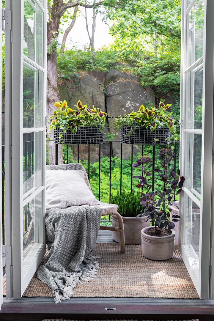En liten, koselig møblert balkong med en lenestol og flere planter, blant annet i Korbos balkongkurv.