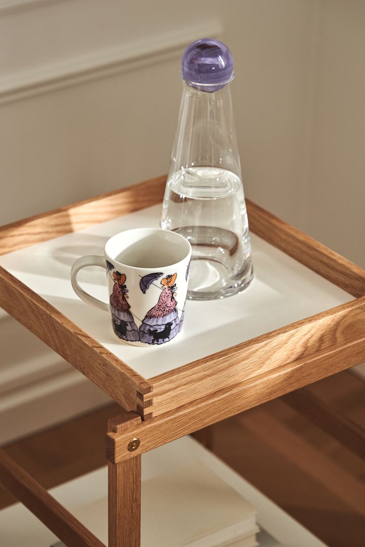med Elsa Beskow-motivet Tante Gredelin fra Design House Stockholm og Fia karaffel i glass med lilla lokk på hylla Frame i eik og hvit.