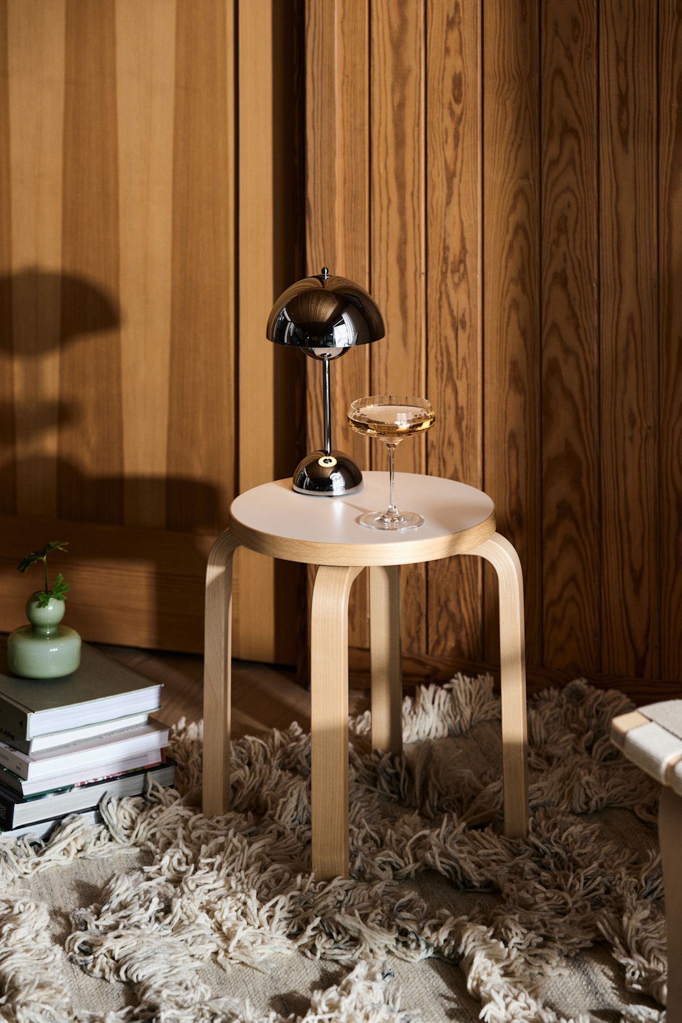 En av de største trendene for 2024 er krom. Her ser du alles favorittlampe, den bærbare bordlampen VP9 Flowerpot i krom, plassert på en krakk ved siden av et glass champagne.