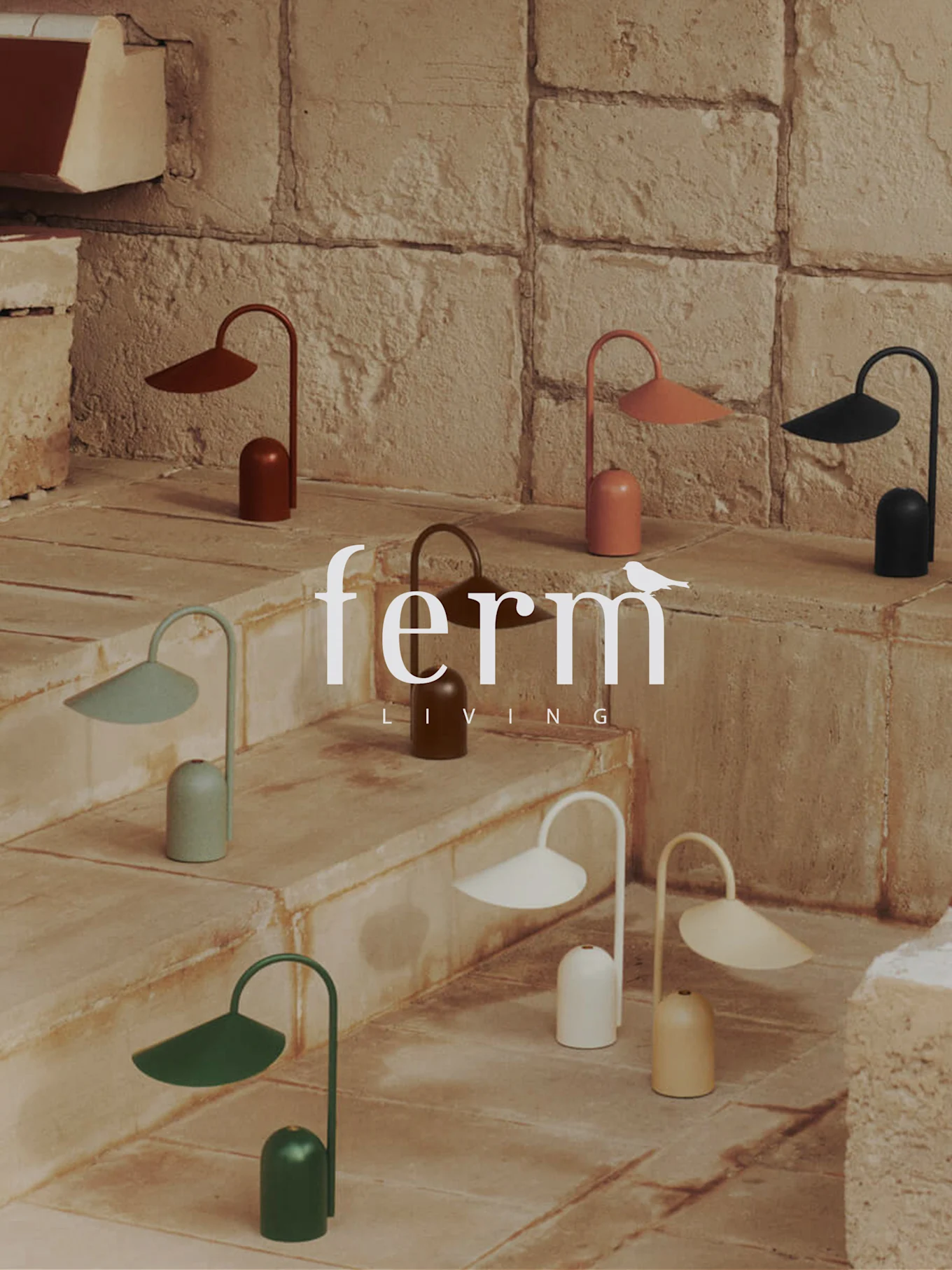 Samling av små, fargerike moderne lamper med klokkebaser og buede skjermer, utstilt på steintrapper. Ferm Living-logo.