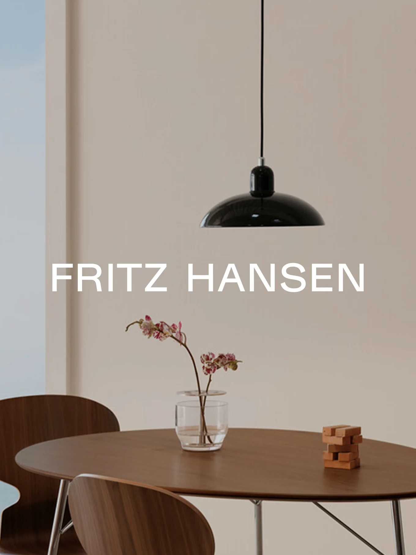 FRITZ HANSEN tekst. Moderne interiør: svart pendellampe, rundt trebord, stoler, orkidé i vase og treklosser.
