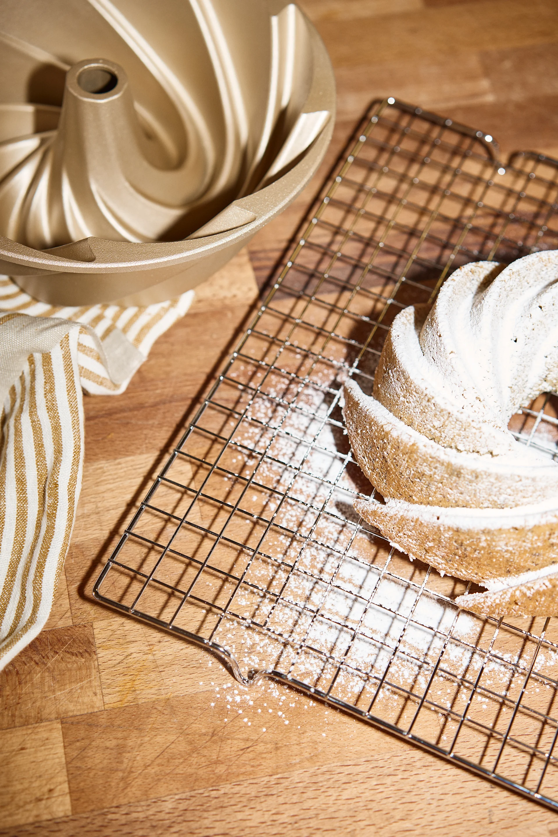 En gyllen bundtform, et stripete håndkle og en bundtkake dynket med melis på en avkjølingsrist.