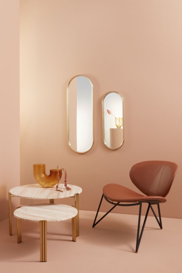 Stilig stue i ferskenfargede toner på veggene, speil med messingkanter og en lekker lenestol i skinn - alle aktuelle trender innen interiørtrender 2023.