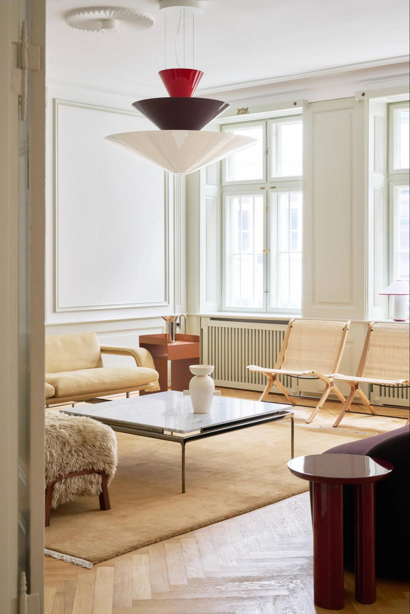 Et moderne stuemiljø med en lagdelt pendellampe, lys gul sofa, flettede stoler og marmor salongbord.