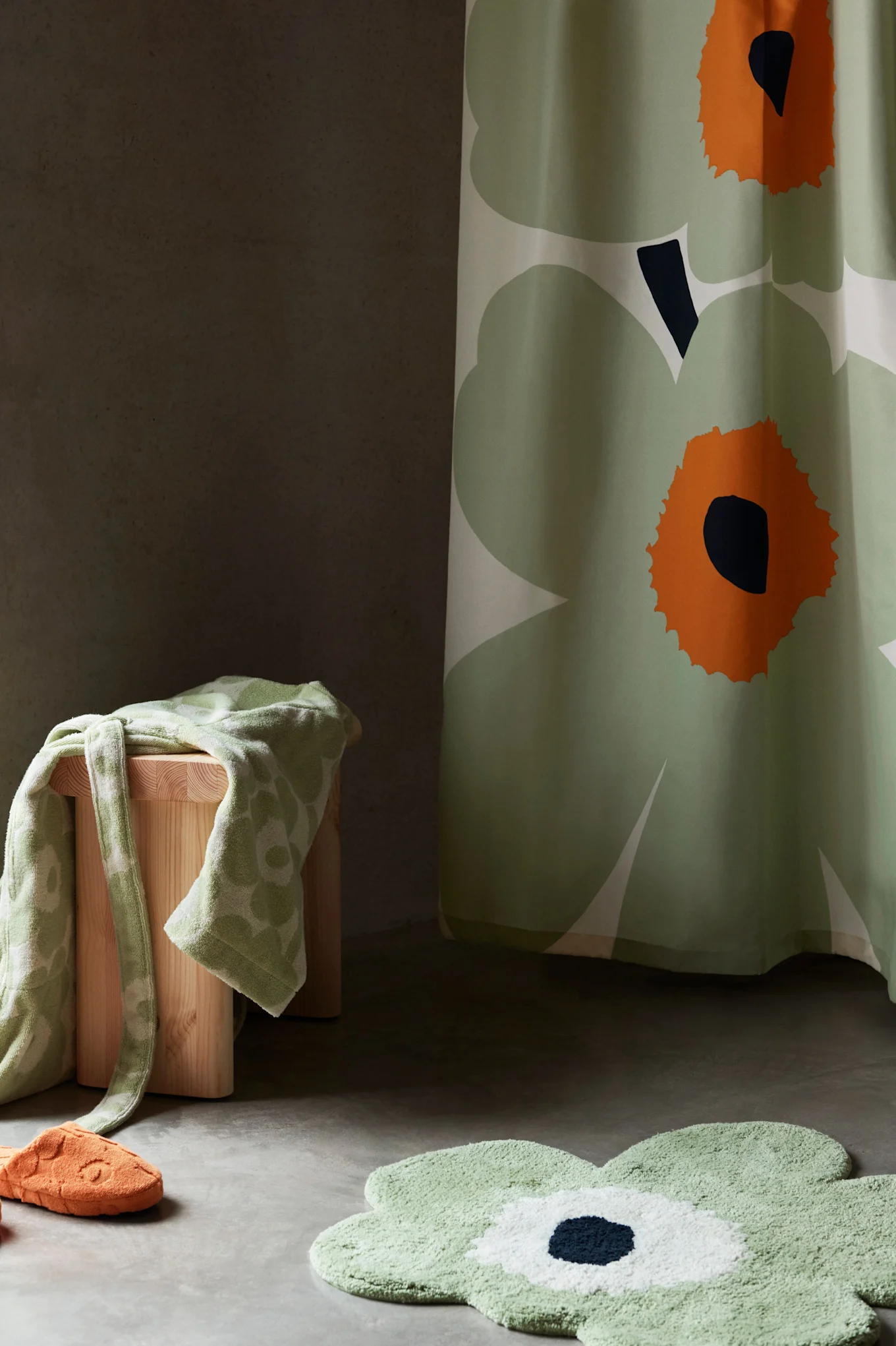 Baderomsinnredning med grønt blomsterdusjforheng, badematte, håndkle på krakk og oransje tøffel.