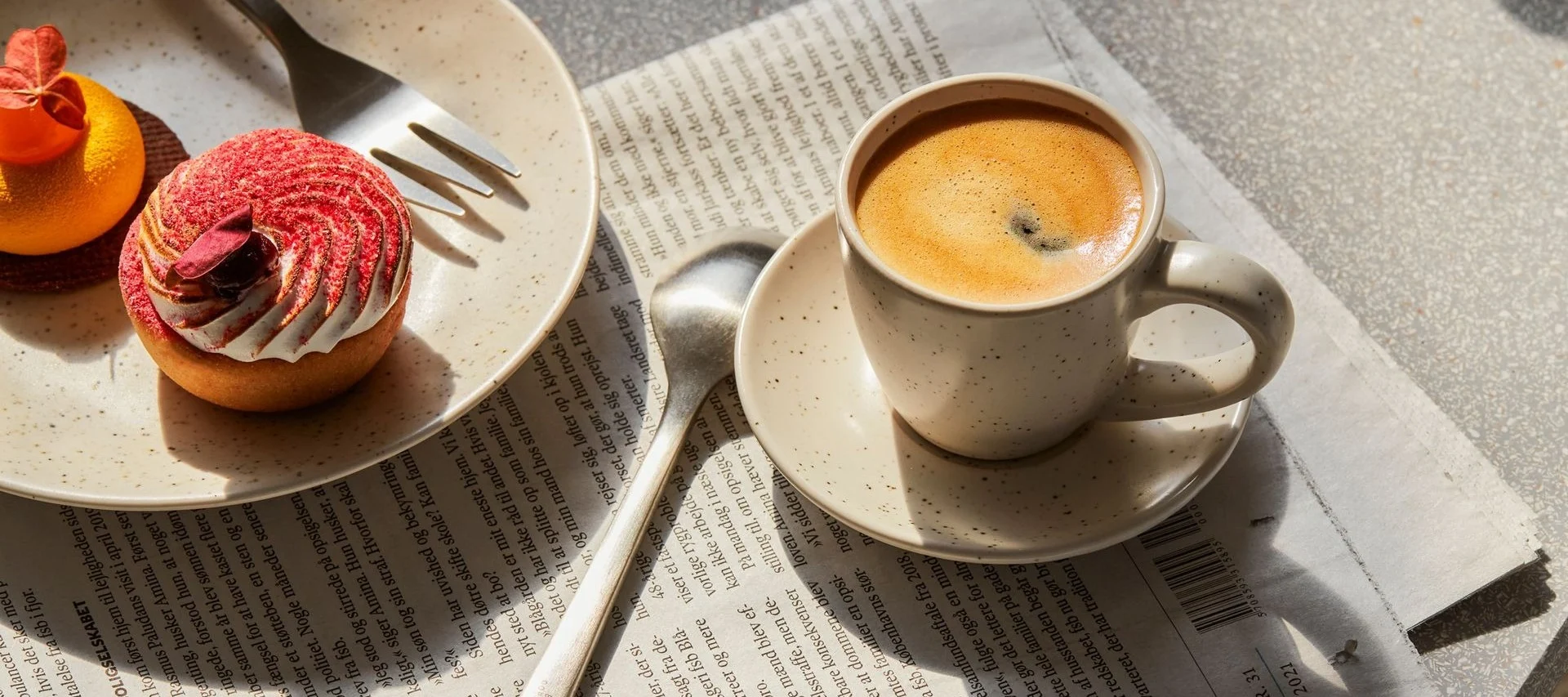 Kaffekopp og to bakverk, en rød terte og en oransje, på en avis.
