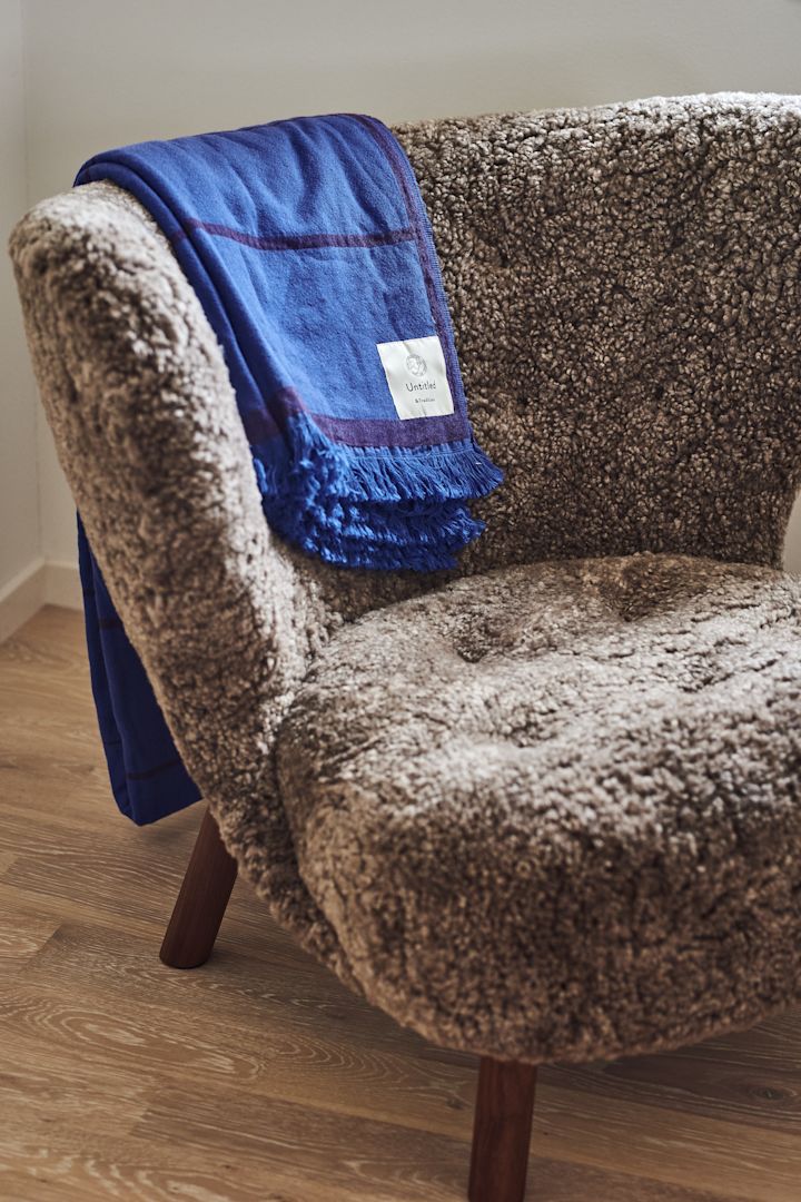 Her ser du loungestolen Lille Petra i en fluffy saueskinnsvariant med det blå Untitled-kastet trukket over toppen, begge fra &Tradition.