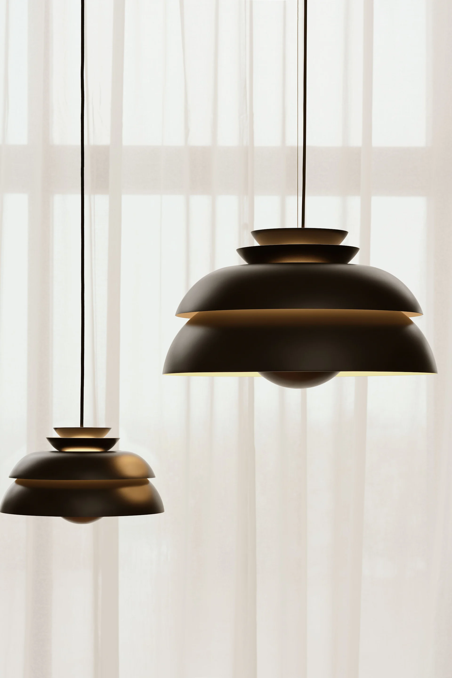 Den svarte Concert-pendellampen fra Fritz Hansen henger foran et vindu med gardiner.