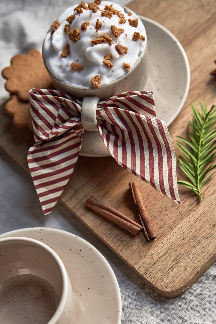 Server en enkel juledrink med kanel, kaffe, pepperkaker i en Freckle-kopp fra Scandi Living sammen med Lines-serviett fra Cooee Design i form av en rosett. 
