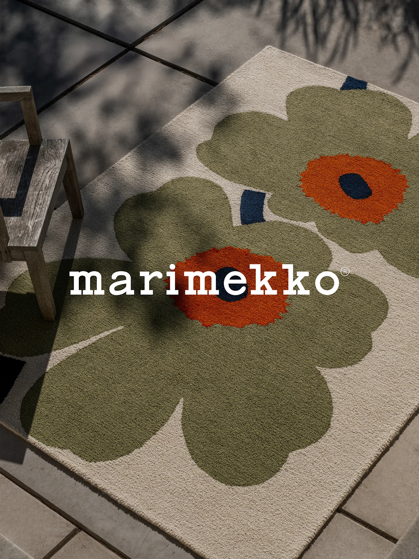 Marimekko-teppe med stort grønt og oransje blomstermønster på en uteplass med en trestol.
