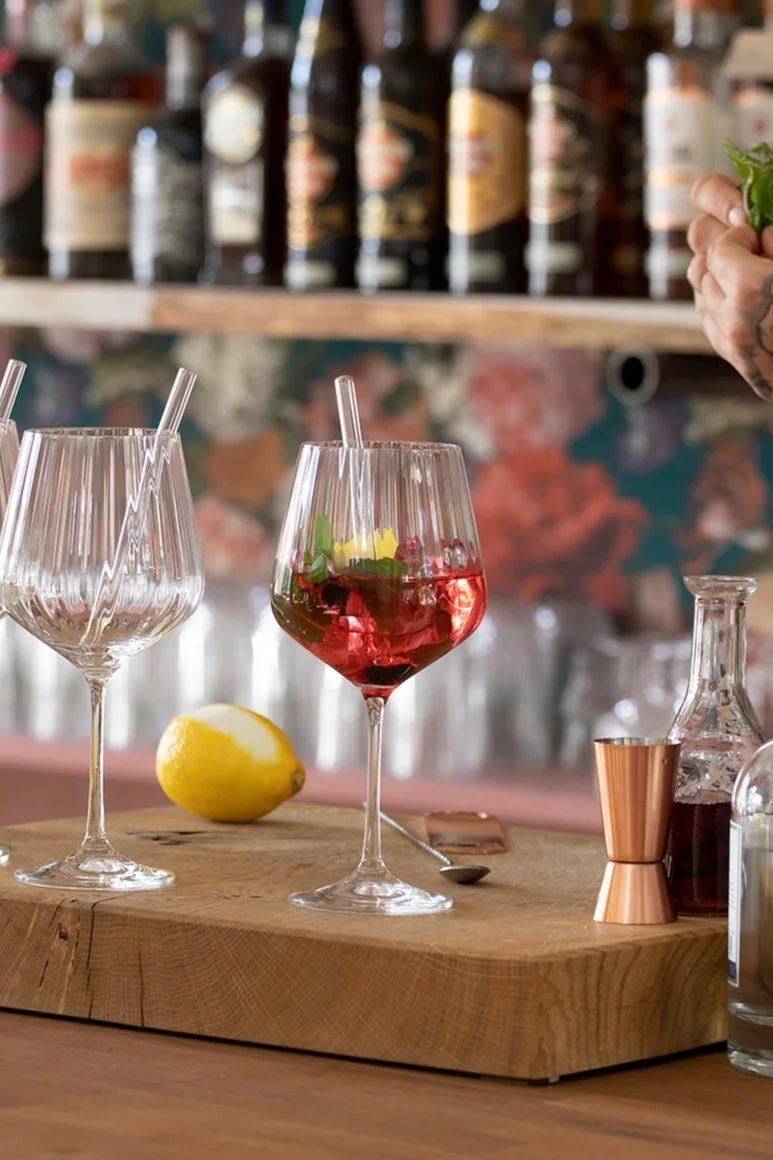 En mocktail i et Feel Good G&T-glass fra Nachtmann står på et trebord foran en bar.