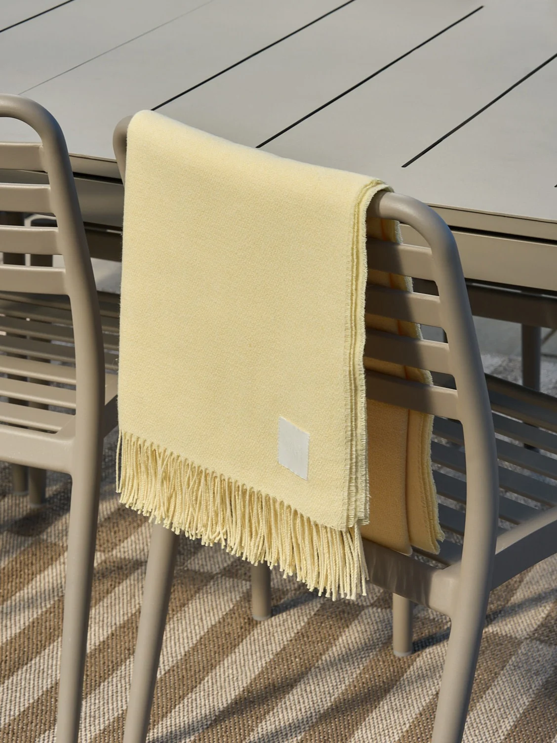 Lys gul pledd med frynser drapert over en beige utendørsstol.