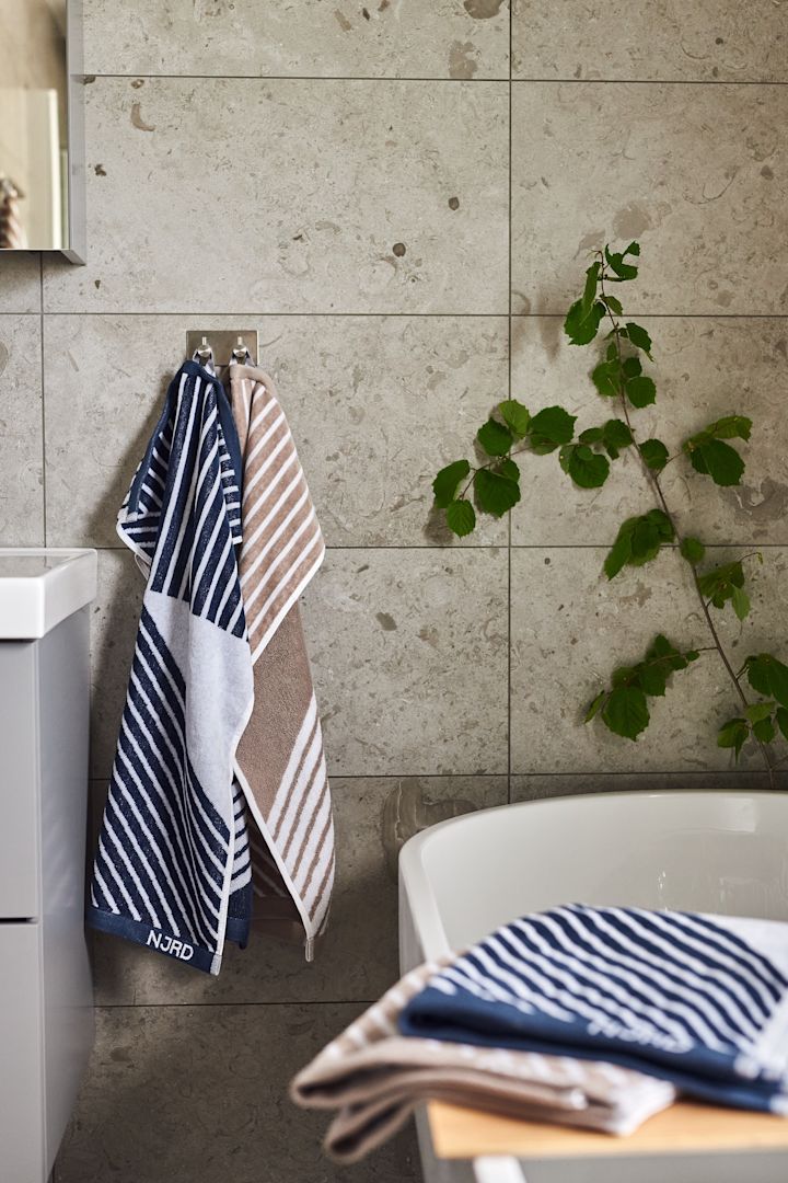 Blått og beige-stripete håndklær fra NJRD hengende på bad med beige fliser.