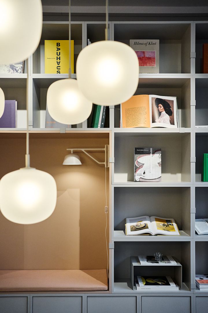 En ryddig hylle dekorert med bøker, med flere Rime-pendellamper fra Muuto hengende i forgrunnen.