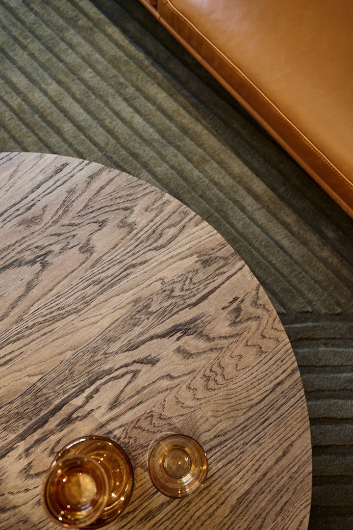 Et sofabord med mørkebrunt bordplate står foran en sofa, med ulike ravfargede glass fra Raise-kolleksjonen til Muuto på toppen.